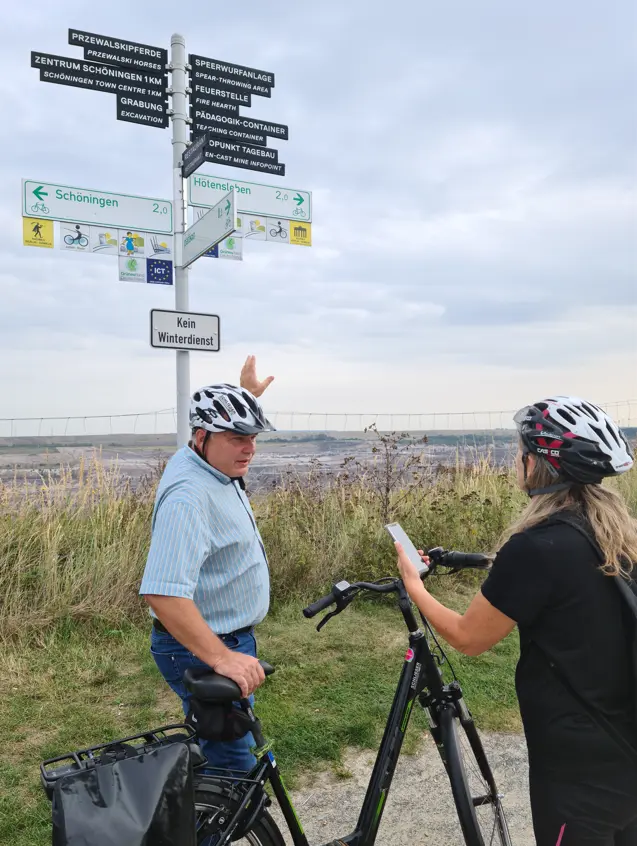 Eine Mann mit Fahrrad zeigt auf einen Wegweiser.