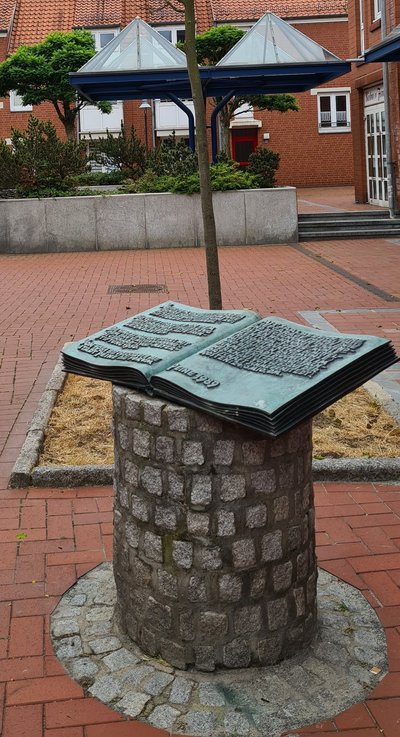 Man blickt auf den Bronzestich enes Buches. Dieser sitzt auf einer gemauerten Säule auf.