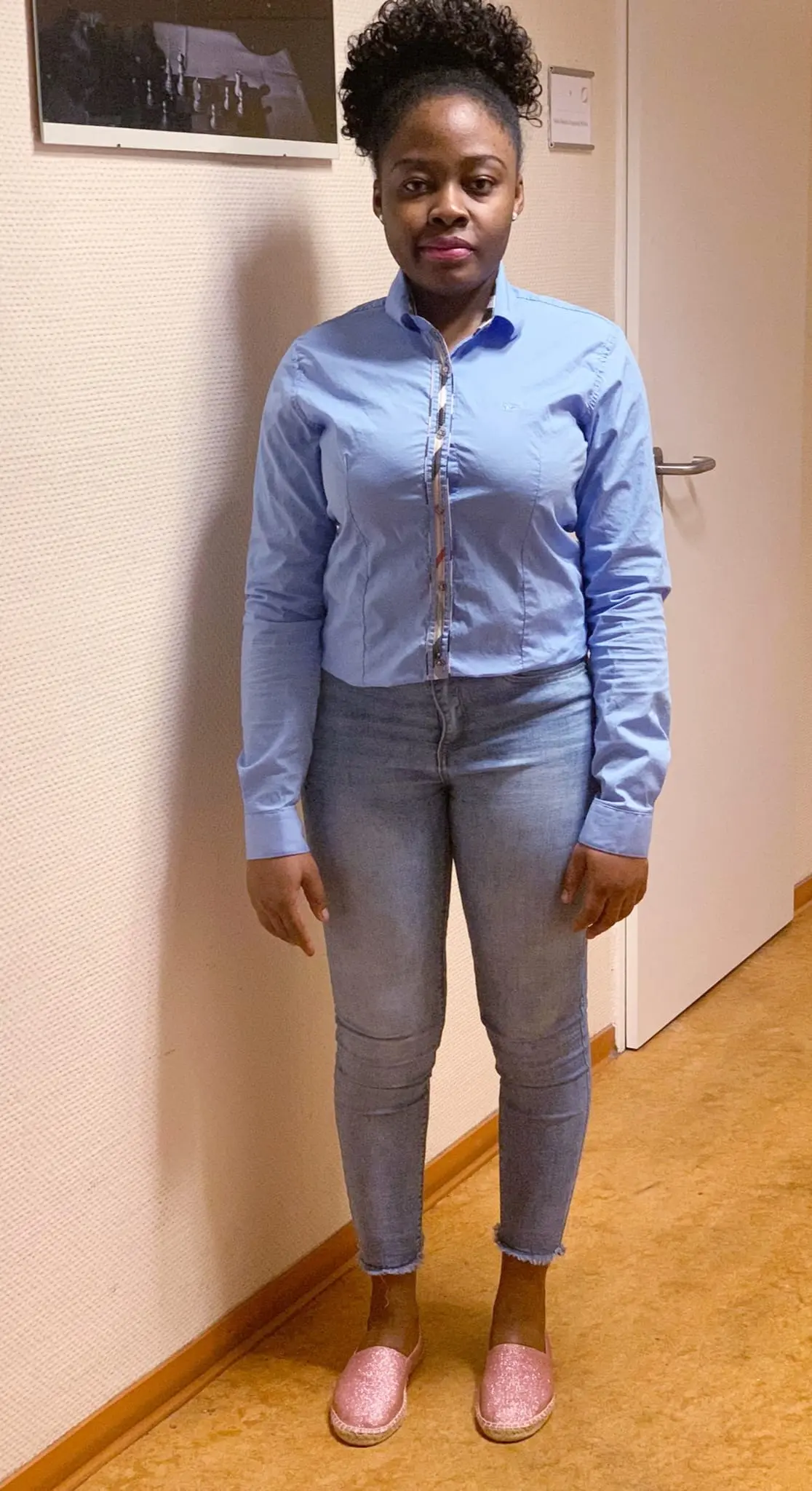 Eine dunkelhäutige Frau steht in einem hellen Flur.