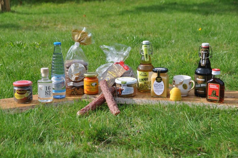 Verschiedene Harzer Produkte, etwa Honig und Bier, stehen auf einem Brett auf einer grünen Wiese.