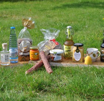 Verschiedene Harzer Produkte, etwa Honig und Bier, stehen auf einem Brett auf einer grünen Wiese. (Bildrechte: Harzer Tourismusverband)