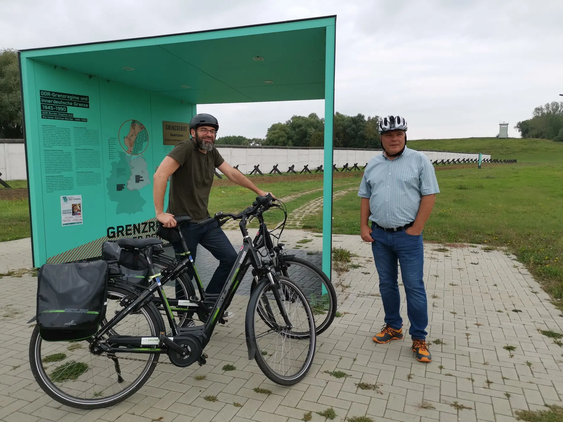 Zwei Radfahrer vor einer grünen Infotafel.