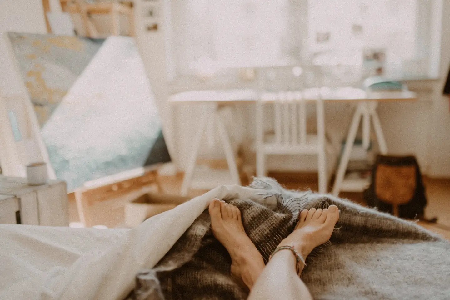 Person liegt barfuß auf einem Bett, im Hintergrund ein Wohnzimmer.