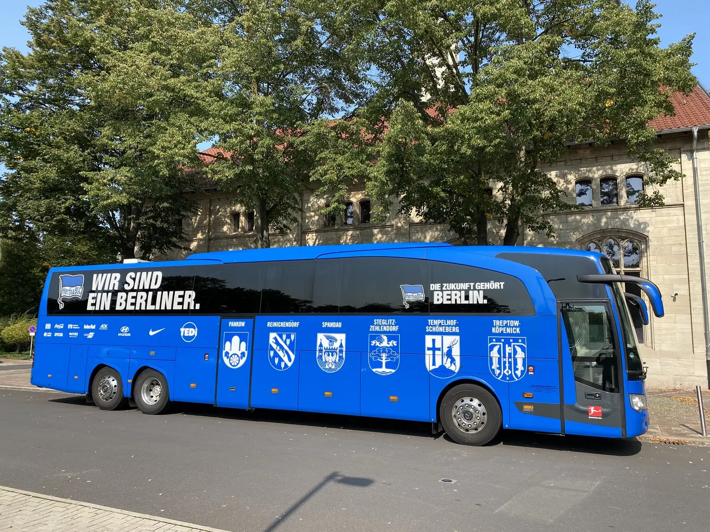 Ein blauer Reisebus vor einem Luxushotel.