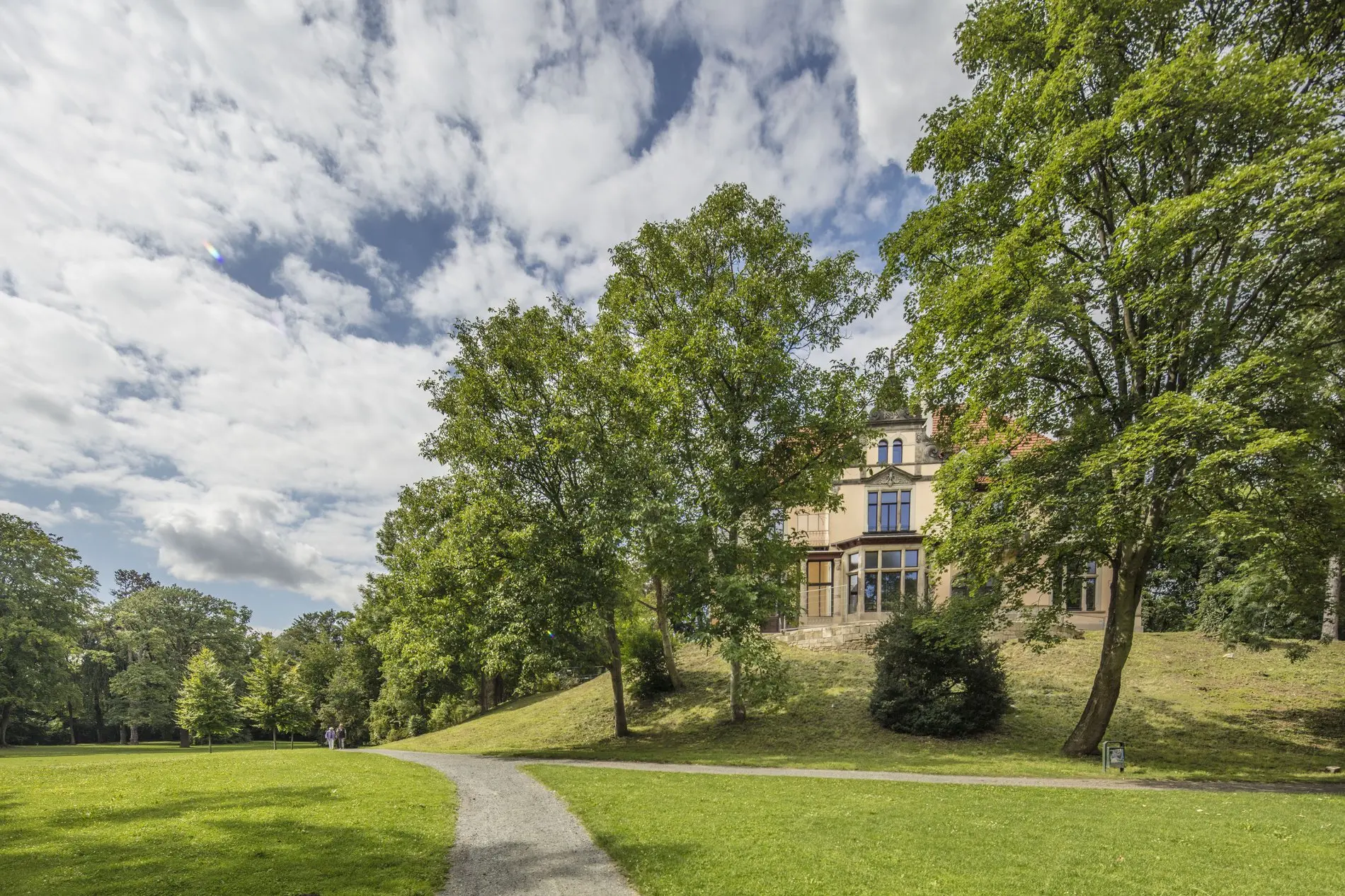 Ein Park in Wolfenbüttel mit einem Fußweg, im Hintergrund eine Villa.
