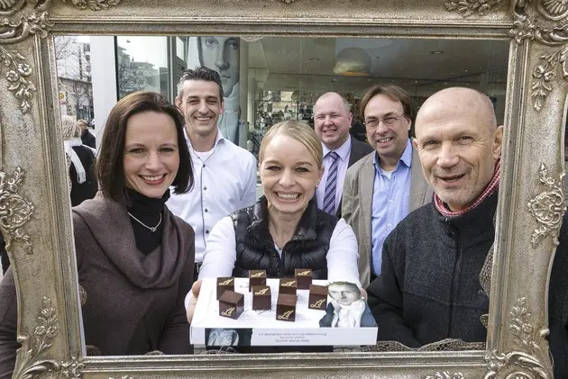 Eine Konditorin präsentiert ein Stück Konfekt. Im Hintergrund mehrere Leute.