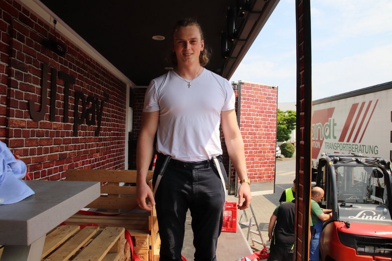 Ein junger, kräftiger Mann steht im offenen Anhänger eines Trucks.