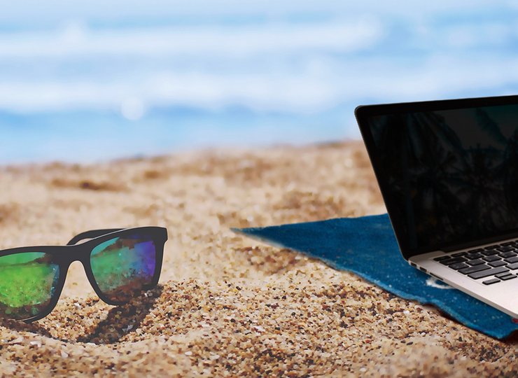 Ein Laptop und eine Sonnenbrille am Strand.