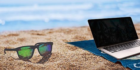Ein Laptop und eine Sonnenbrille am Strand.