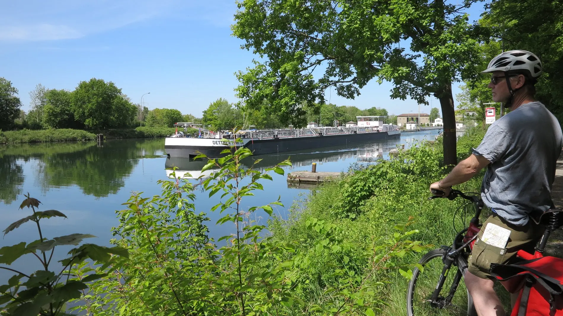 Ein Kanal vom grünen Ufer aus gesehen, rechts im Bild ein Radfahrer.