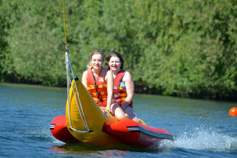 Zwei Frauen sitzen auf einem bananenförmigen Luftkissen im Salzgittersee.