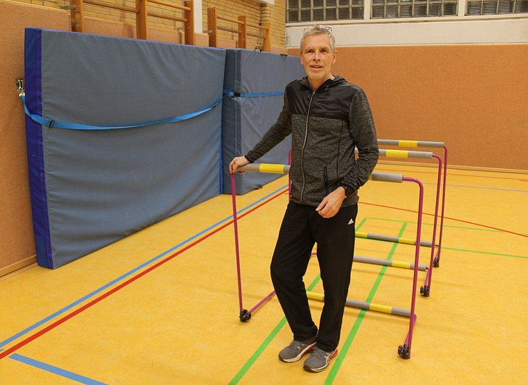 Ein Leichtathletik-Trainer steht vor drei Hürden in einer Halle.