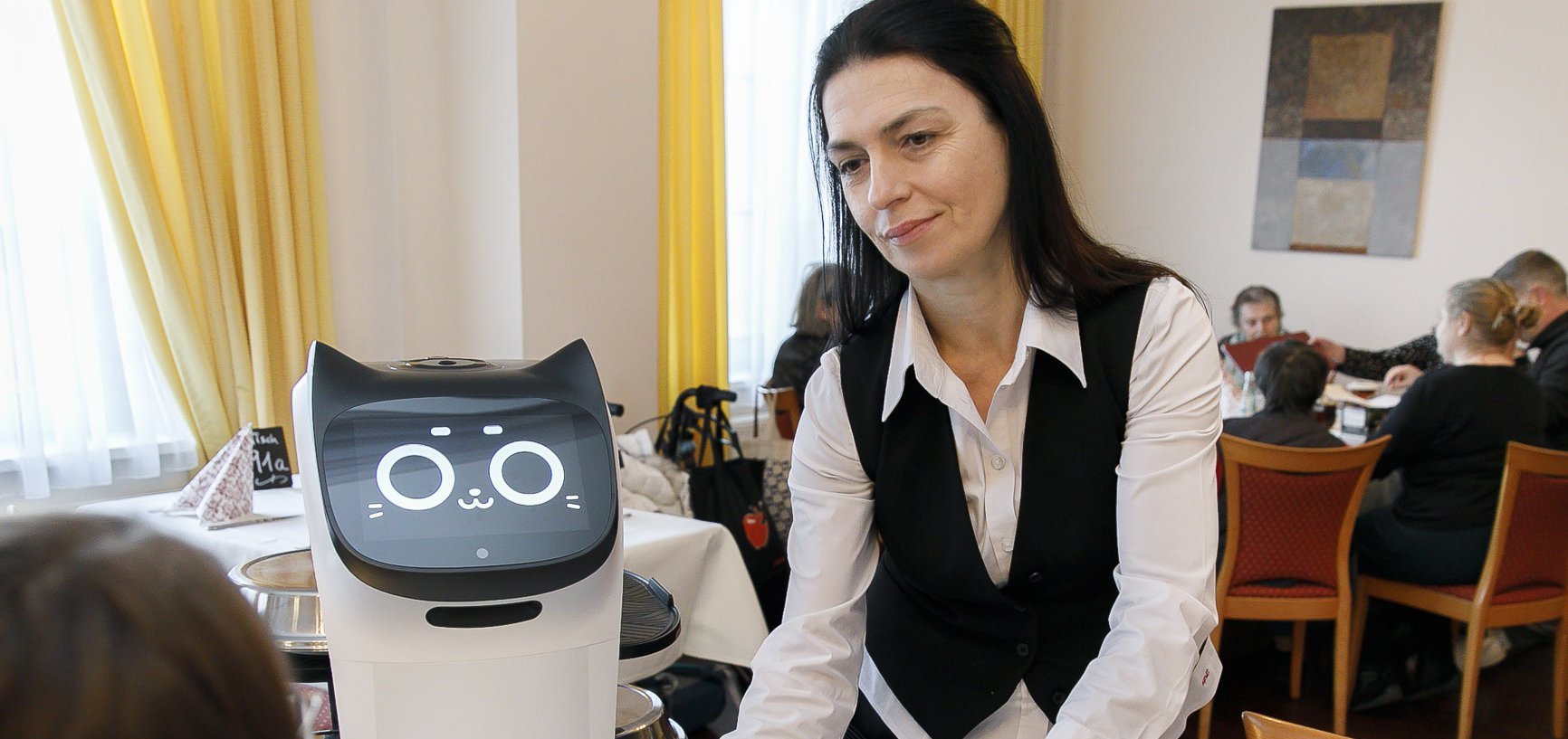 Eine Kellnerin serviert Essen, ein Roboter steht daneben.