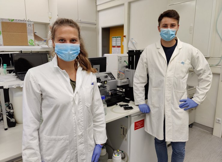 Zwei junge Wissenschaftler im Labor mit Mundschutz und Kittel. 