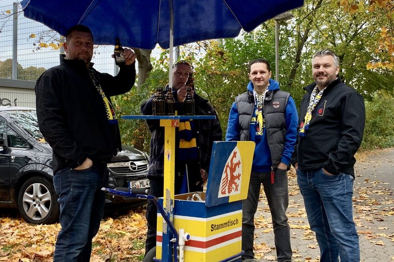 Vier Männer unter einem blauen Schirm in Eintracht-Montur.