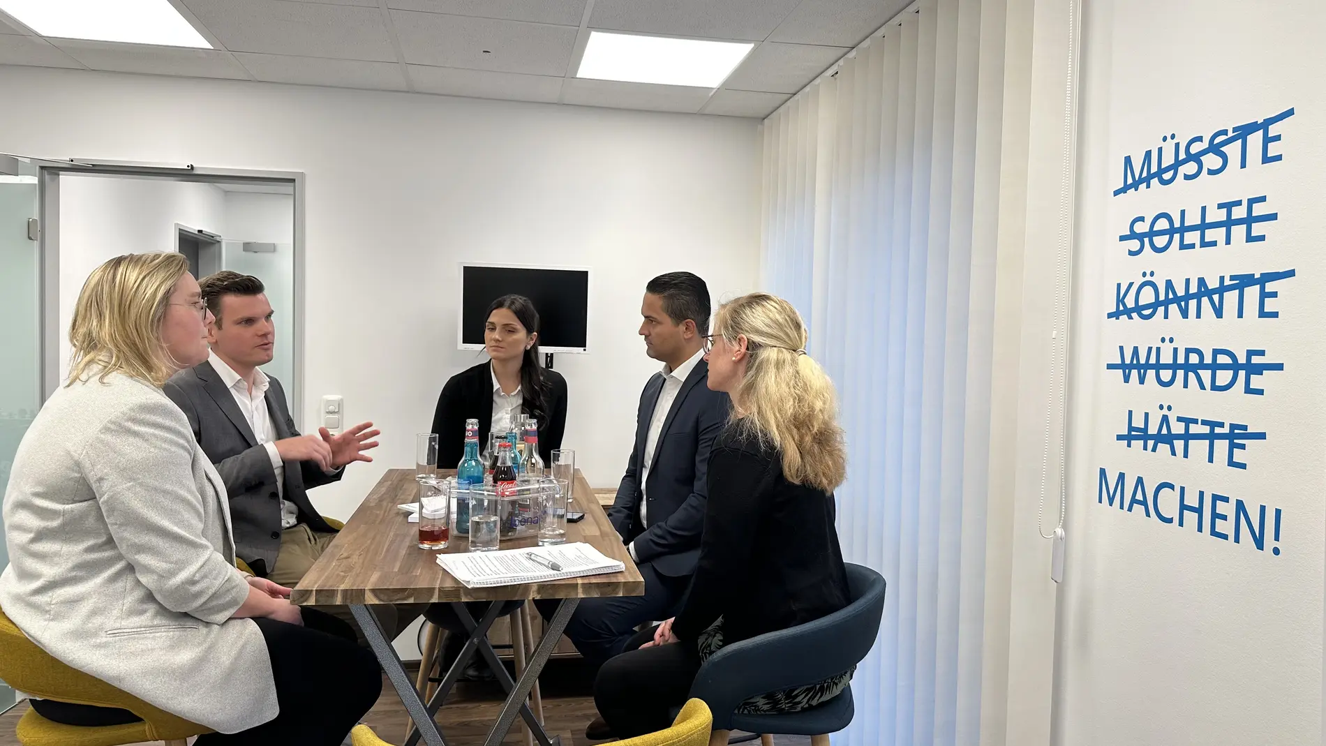 Fünf Personen sitzen an einem Tisch und unterhalten sich.