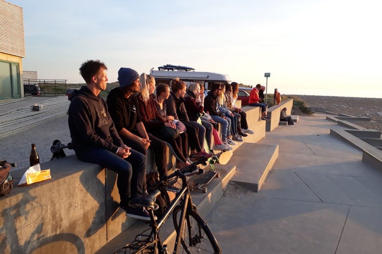 Junge Leute sitzen auf einer Mauer an einem Meer.