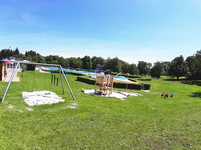Spielgeräte auf dem Gelände des Freibads Räbke unter blauem Himmel. 