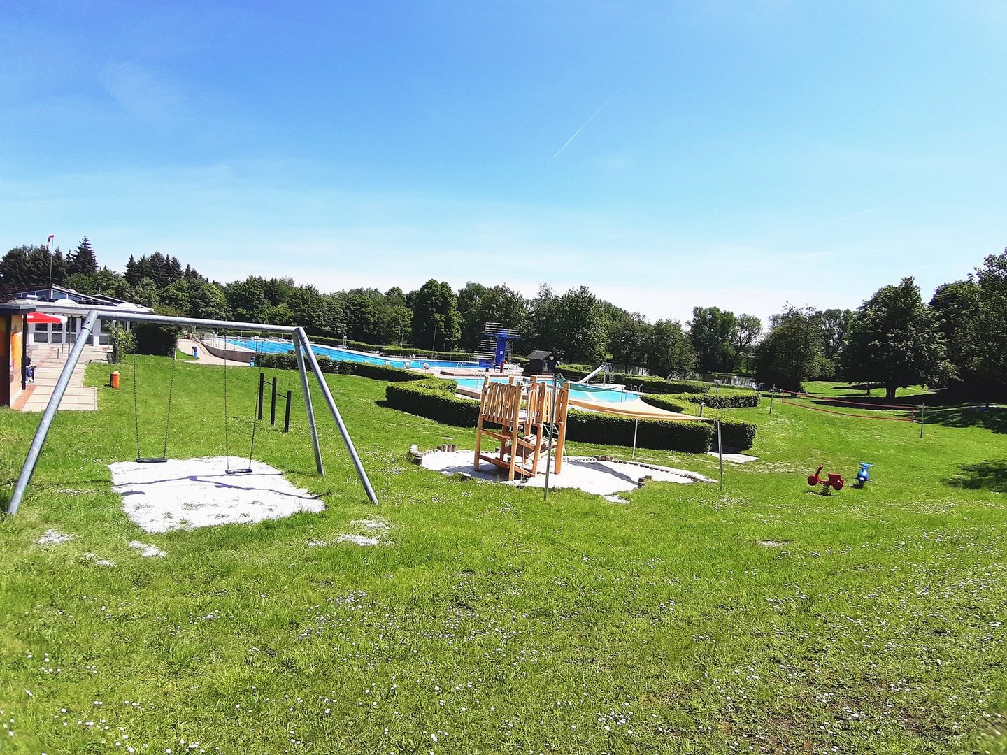 Spielgeräte auf dem Gelände des Freibads Räbke unter blauem Himmel. 