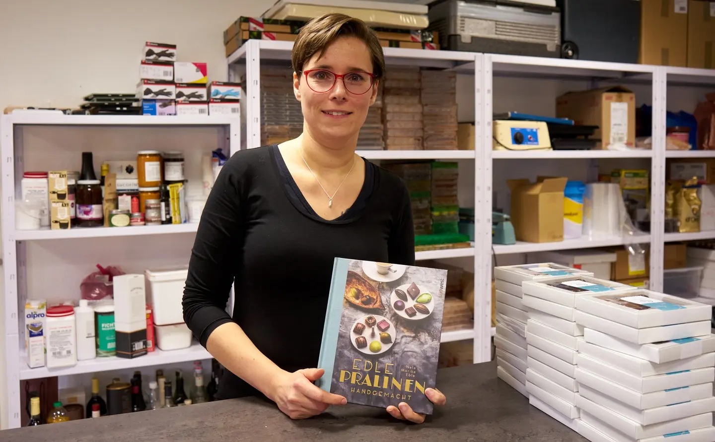 Eine Frau hält ein Buch vor sich in die Kamera. Es geht um Pralinen.