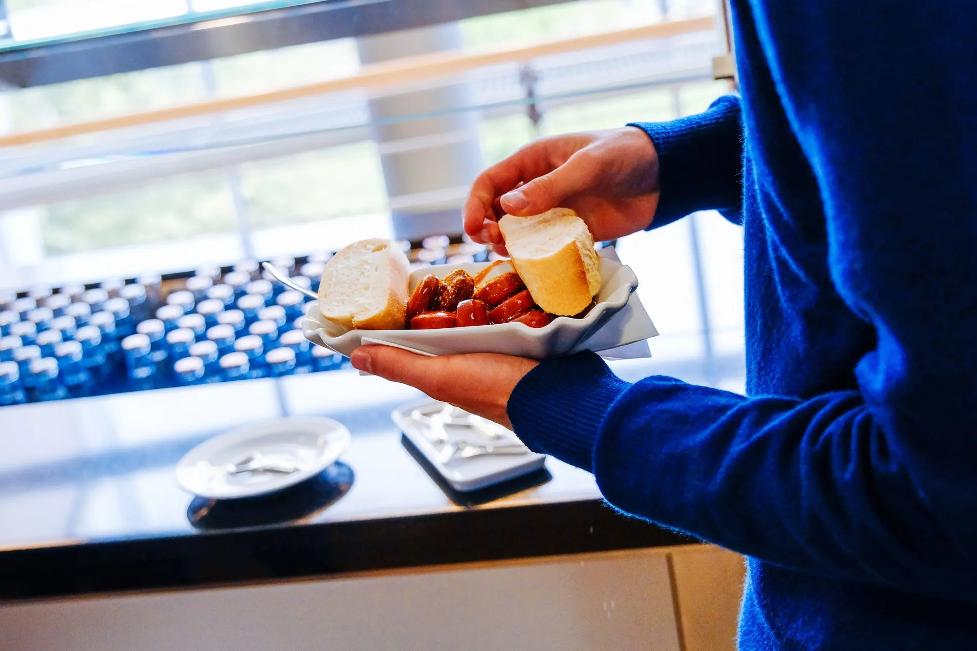 Ein Mitarbeiter in der Kantine hält einen Pappteller mit Currywurst in der Hand.