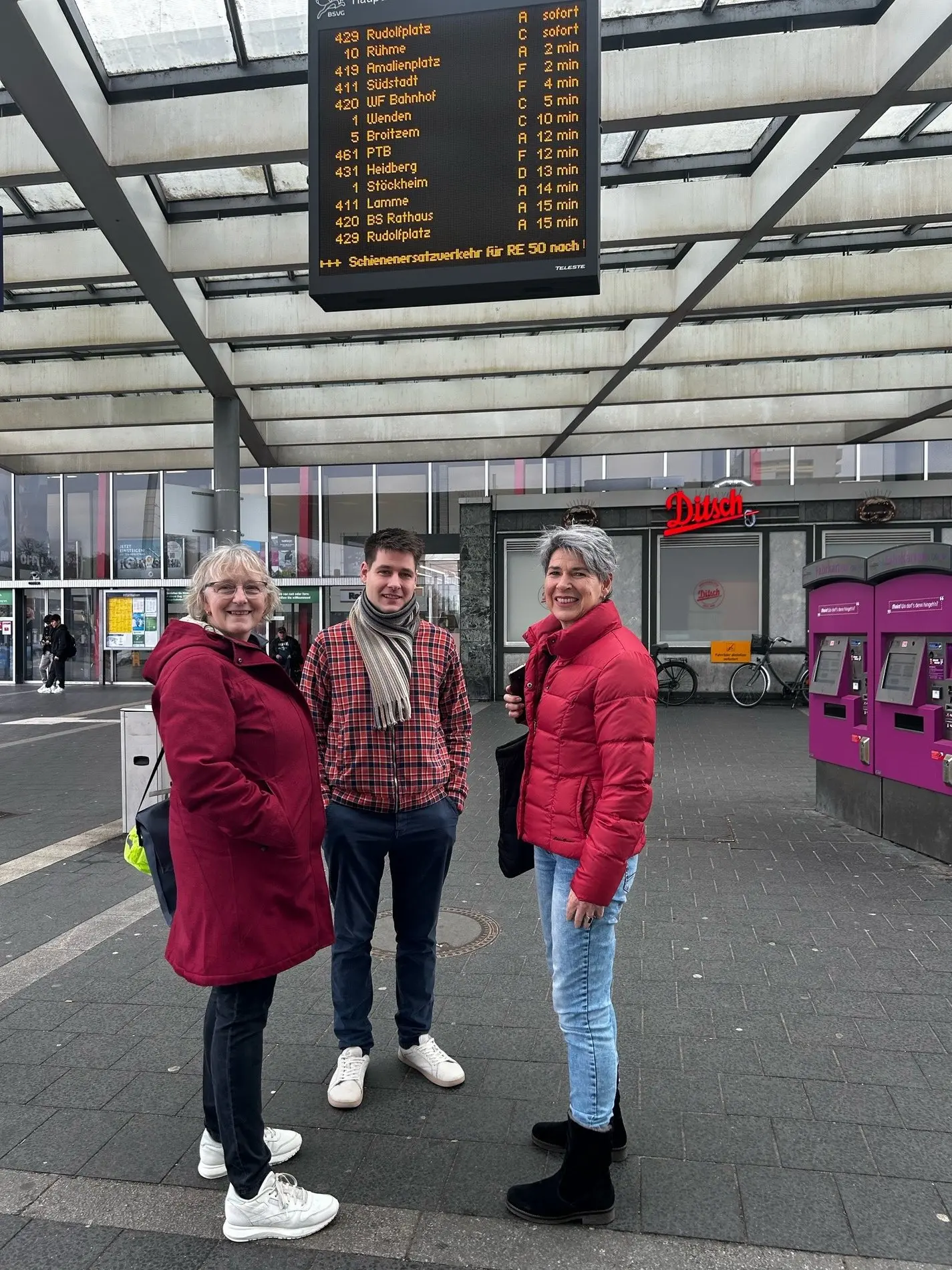 Susanne Koch, Jasper Märtens und Beate Ziehres unter dem DFI-Monitor am Bahnhof in Braunschweig. 