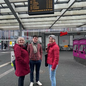Susanne Koch, Jasper Märtens und Beate Ziehres unter dem DFI-Monitor am Bahnhof in Braunschweig.