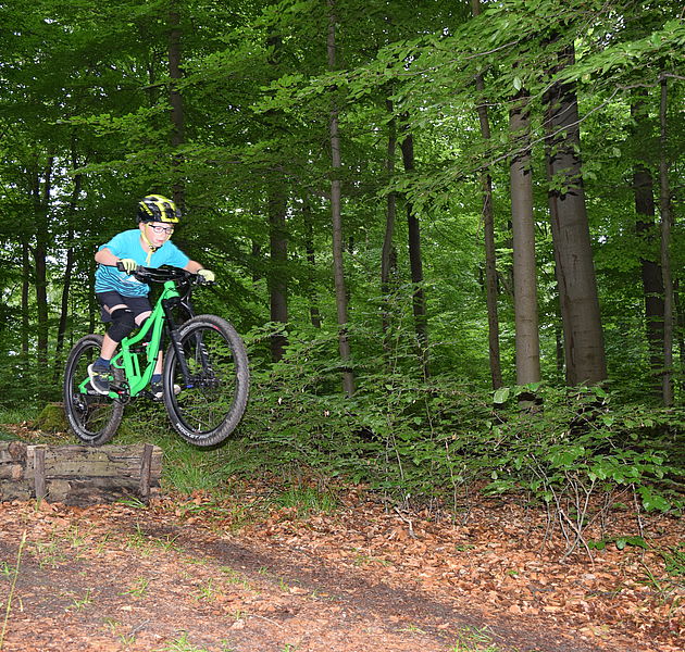 Ein Kind springt mit seinem Mountainbike über einen Hügel im Wald. (Bildrechte: Martina Zingler)