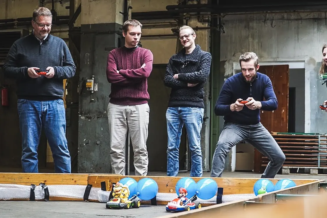 Vier Männer fahren ein Rennen mit ferngesteuerten Fahrzeugen in einer Halle.