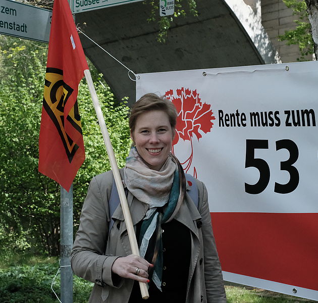 Eine Gewerkschaftlerin mit roter Fahne vor einem Plakat in Braunschweig. (Bildrechte: Meike Buck)