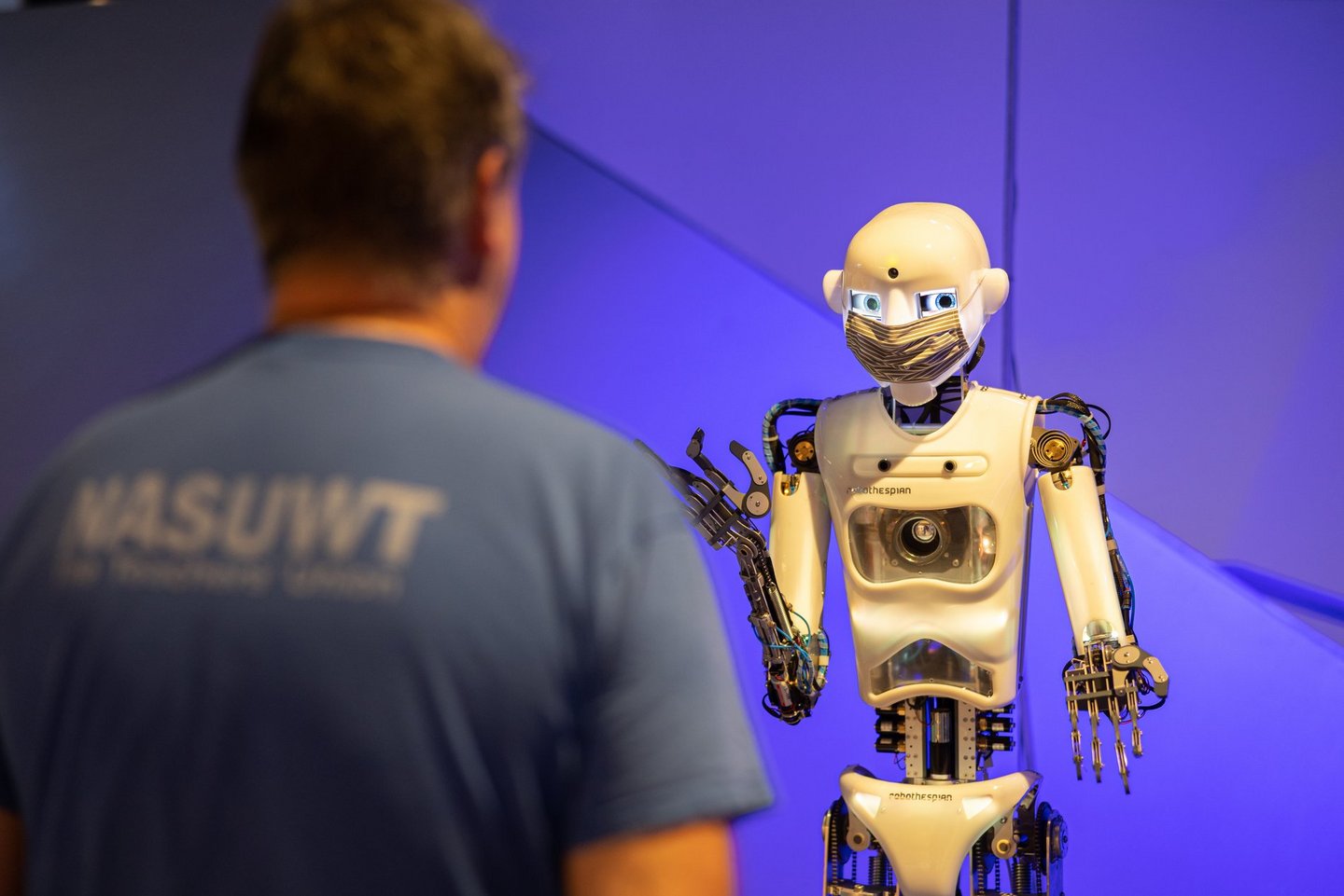 Man blickt auf einen Roboter. Im Vordergrund steht ein Besucher, der sich den Roboter anschaut.