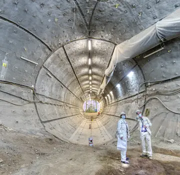 Zwei Mitarbeiter stehen unter der Erde vor einer kreisrunden Öffnung, durch die ein Schlauch verläuft. (Bildrechte: Bundesgesellschaft für Endlagerung.)