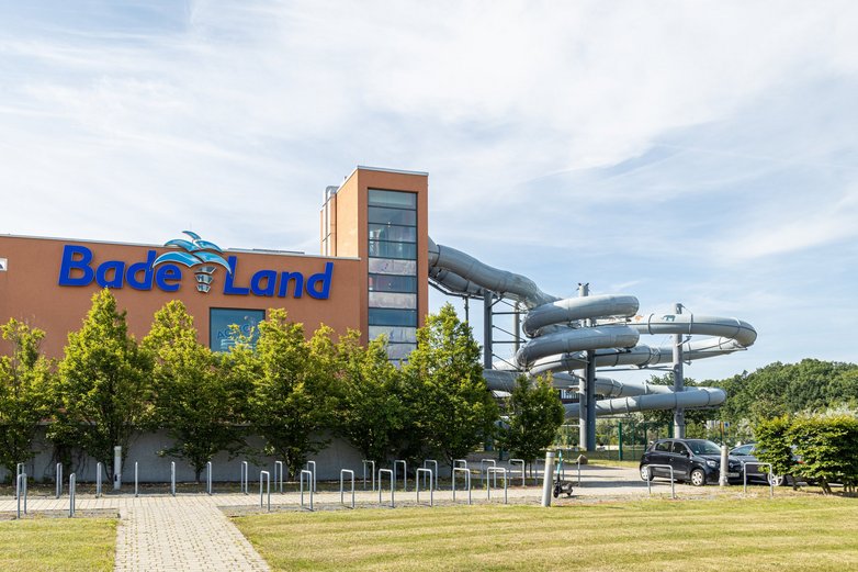 Ein Schwimmbad von Außen. In der rechten Hälfte des Bildes sind mehrere Rutschen zu sehen, die aus dem Hauptgebäude abgehen.