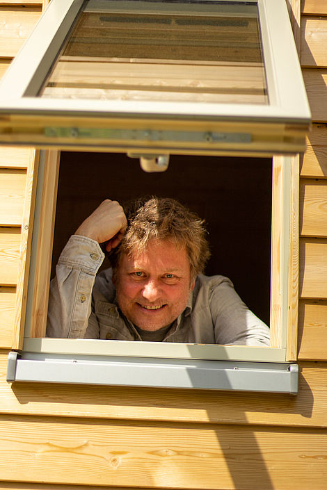 Ein Mann schaut aus einem nach außen hochgeklappten Fenster.