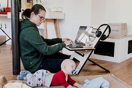 Eine Frau am Laptop, rechts neben ihr liegt ein Baby. 