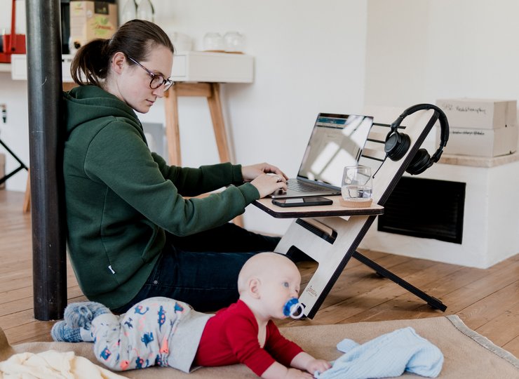 Eine Frau am Laptop, rechts neben ihr liegt ein Baby. 