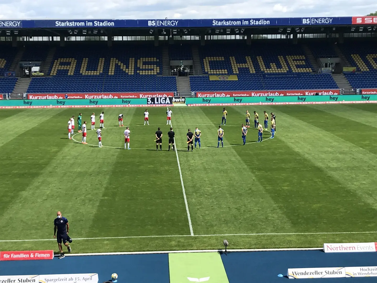 Beide Fußballmannschaften haben sich um den Mittelkreis im Eintracht-Stadion zum gedenken aufgestellt.