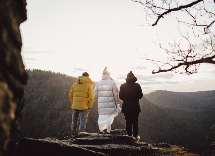 Drei Menschen, von hinten fotografiert, stehen an einer Klippe. Vor Ihnen ein Abgrund, im Hintergrund der Harzer Bergwald.