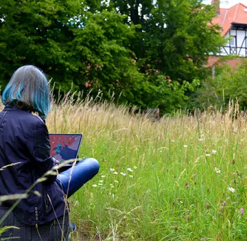 Eine Frau sitzt mit einem Laptop auf dem Schoß in einer Wiese. (Bildrechte: Dreßler Automation)