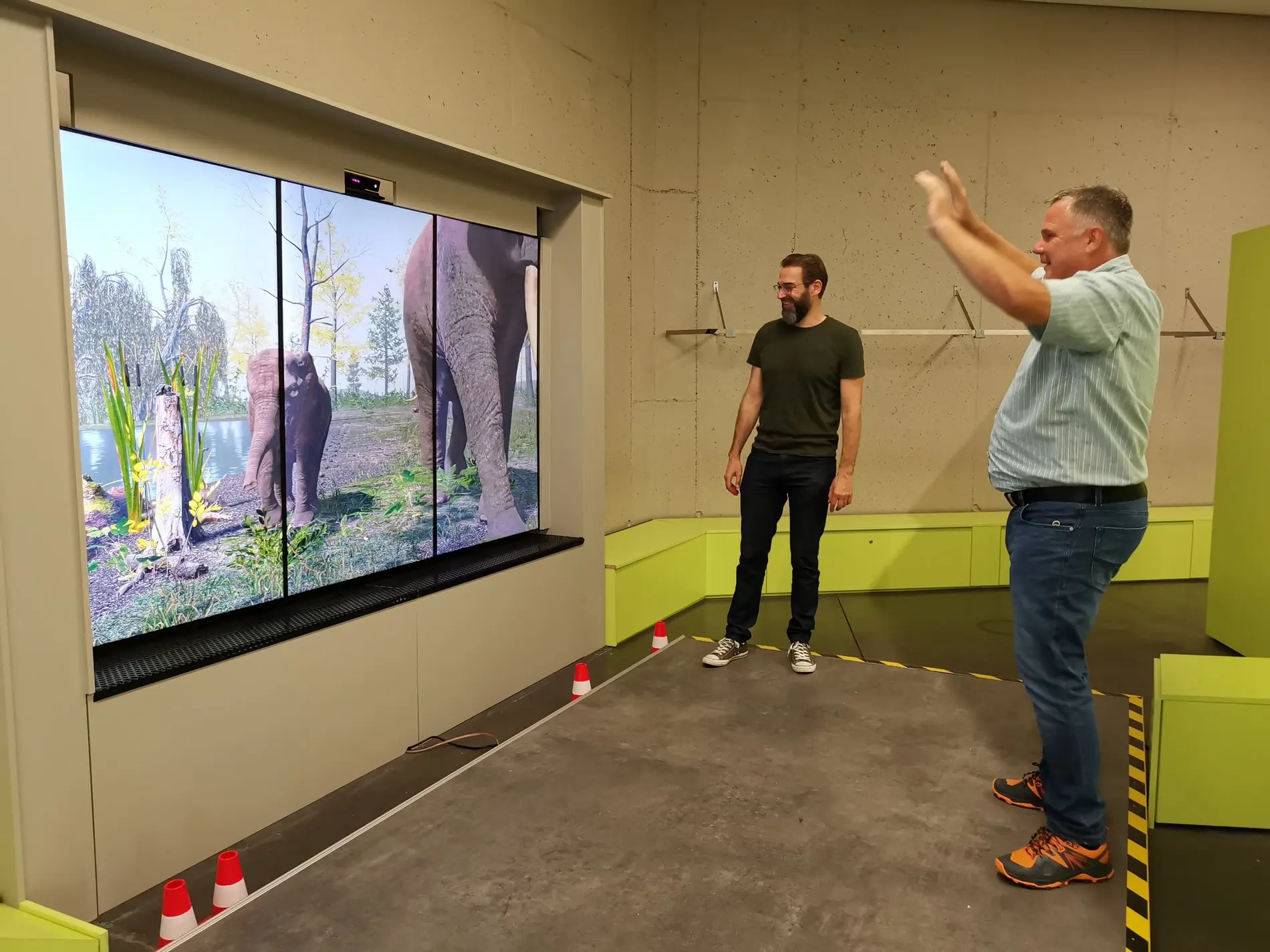 Ein Mann steht vor einem Bildschirm, der Elefanten zeigt.