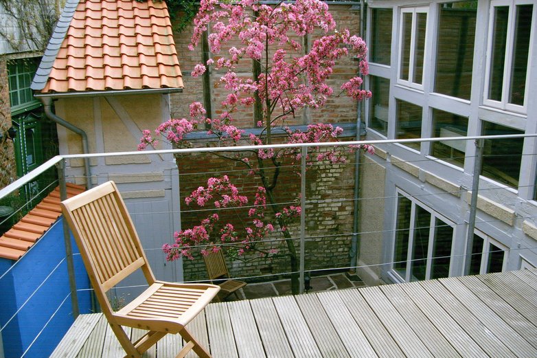 Ein Stuhl auf der Terrasse in einem Hinterhof eines Hauses in Helmstedt vor einem blühendem Baum.