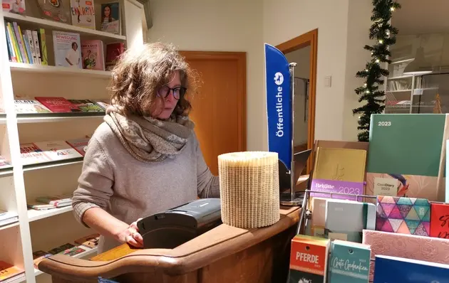 Eine Buchhändlerin steht hinter einer Kasse.