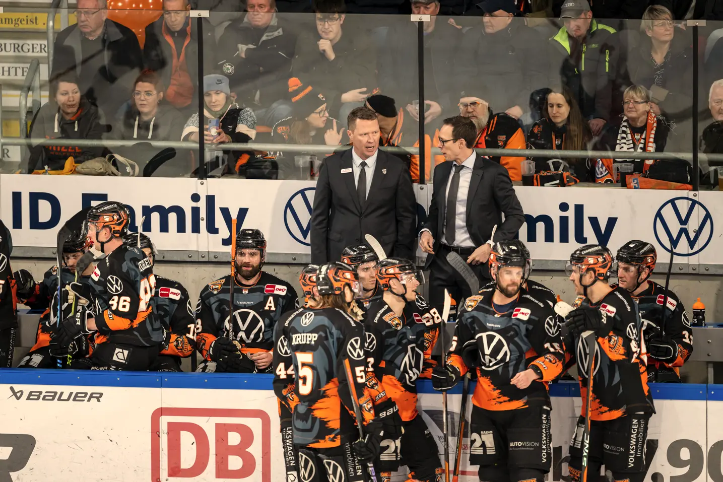 Die Reservebank mit Eishockeyspielern, dahinter die Trainer.