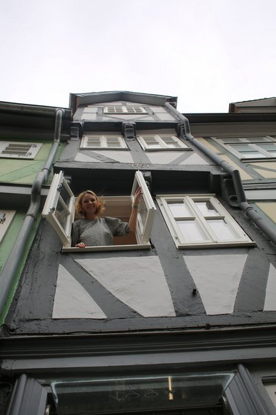 Eine Frau schaut aus dem Fenster eines schmalen Fachwerkhauses.