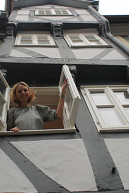 Eine Frau schaut aus dem Fenster eines schmalen Fachwerkhauses.