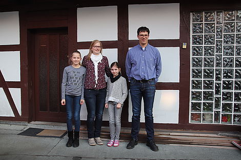 Ehepaar Henkel steht mit seinen beiden Töchtern vor der Außenwand ihres Fachwerkhauses. 