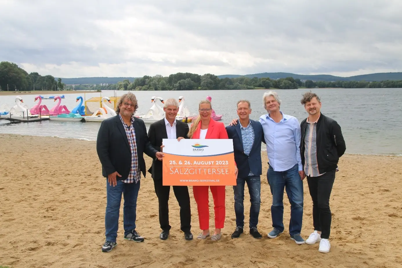 Sechs Leute stehen hinter einem kleinen Plakat auf dem Strand am Salzgittersee.