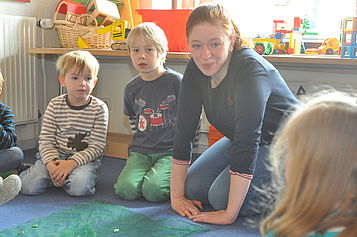 Auf einem blauen Teppich spielen Jakob, Jasper und Joscha mit Jennifer Polo.