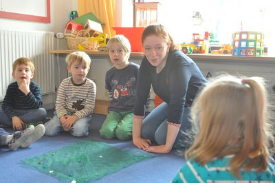 Auf einem blauen Teppich spielen Jakob, Jasper und Joscha mit Jennifer Polo.