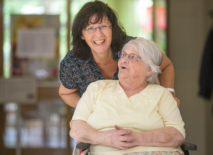 Von einer Pflegerin wird eine Seniorin im Rollstuhl geschoben. 